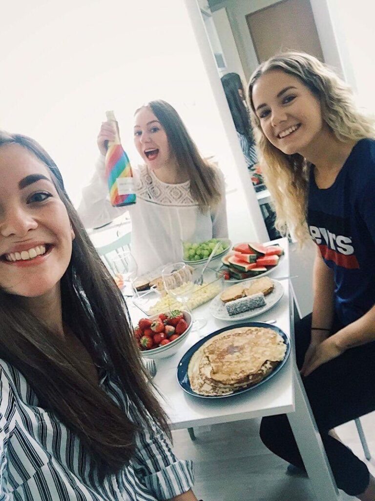 Tre kvinnor ler vid ett bord där det finns pannkakor och cava.