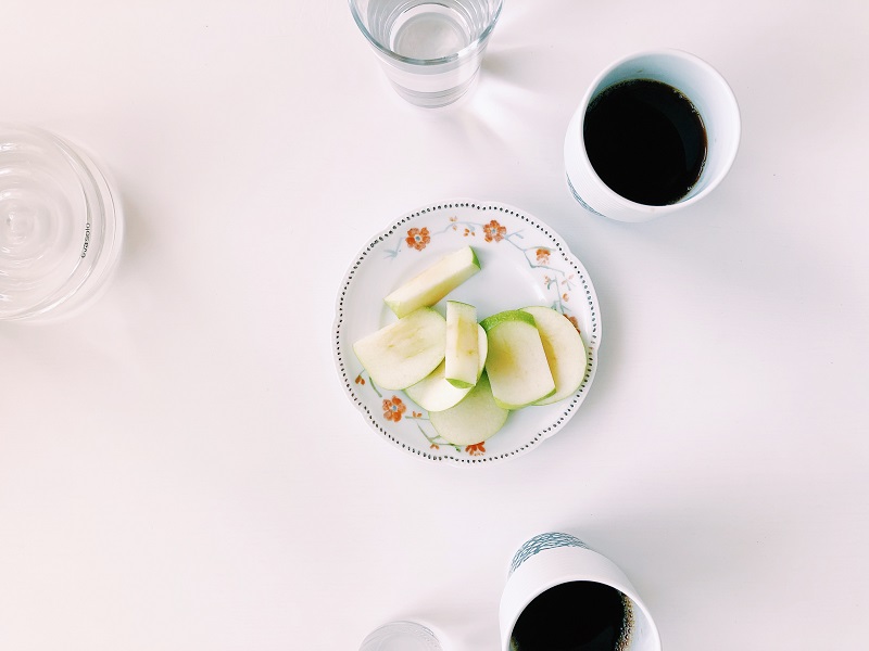 En assiett med skivat äpple på. På bordet står också två koppar kaffe.